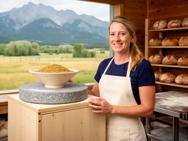 A smiling baker in a cream apron beside a new granite stone grain mill with loaves on shelves behind.